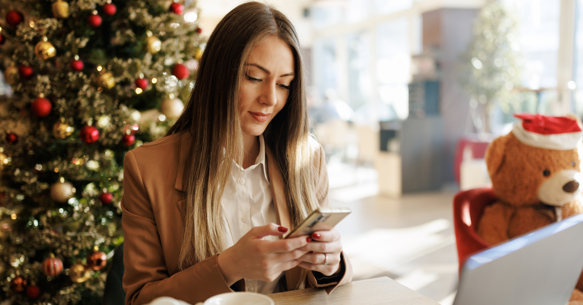 Žena pri vianočnom stromčeku spokojne sleduje mobil, vyžaruje pokoj a radosť zo single sviatočných chvíľ.
